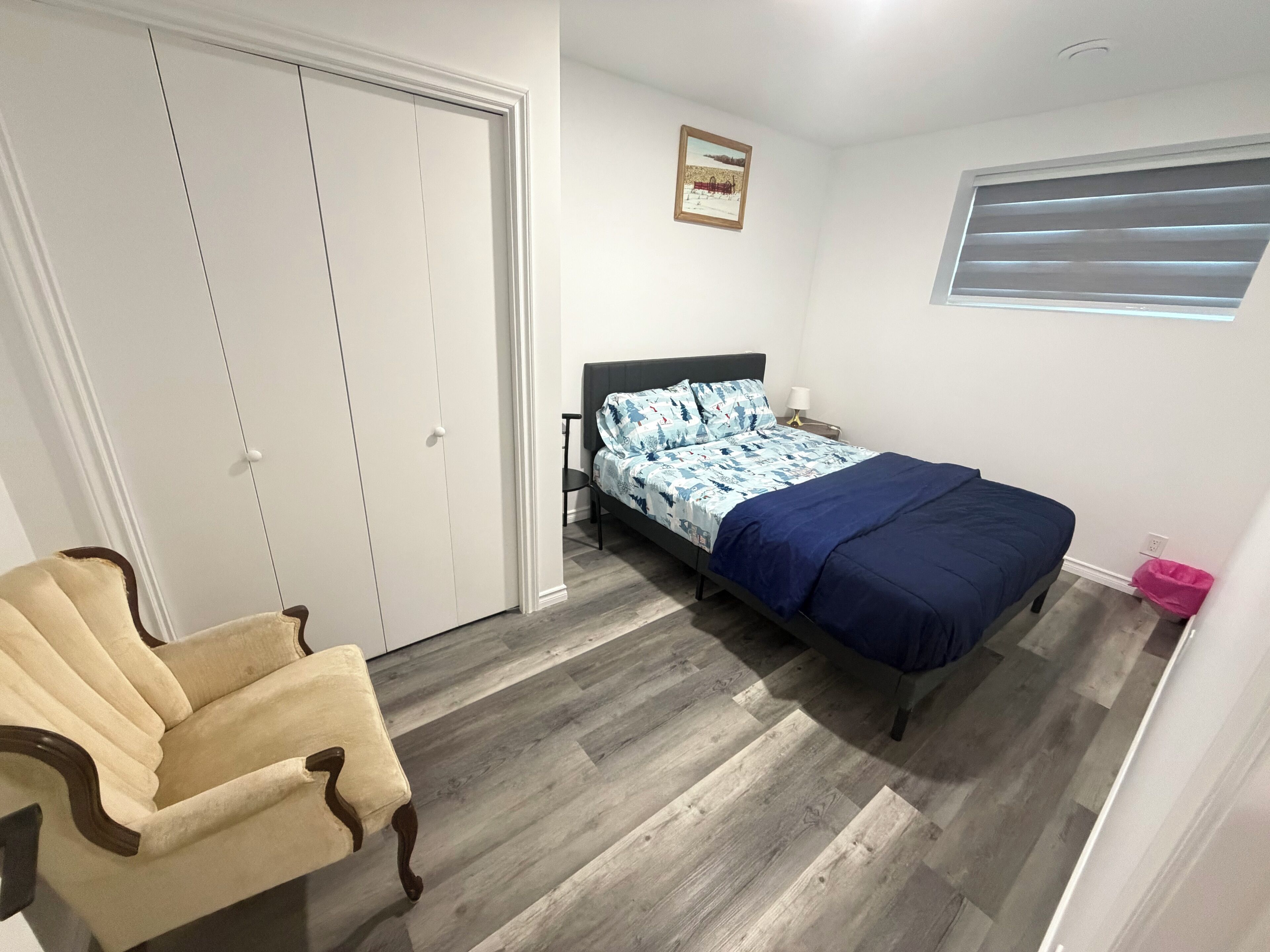 Um quarto com uma cama, uma cadeira, um guarda-roupa e uma janela.