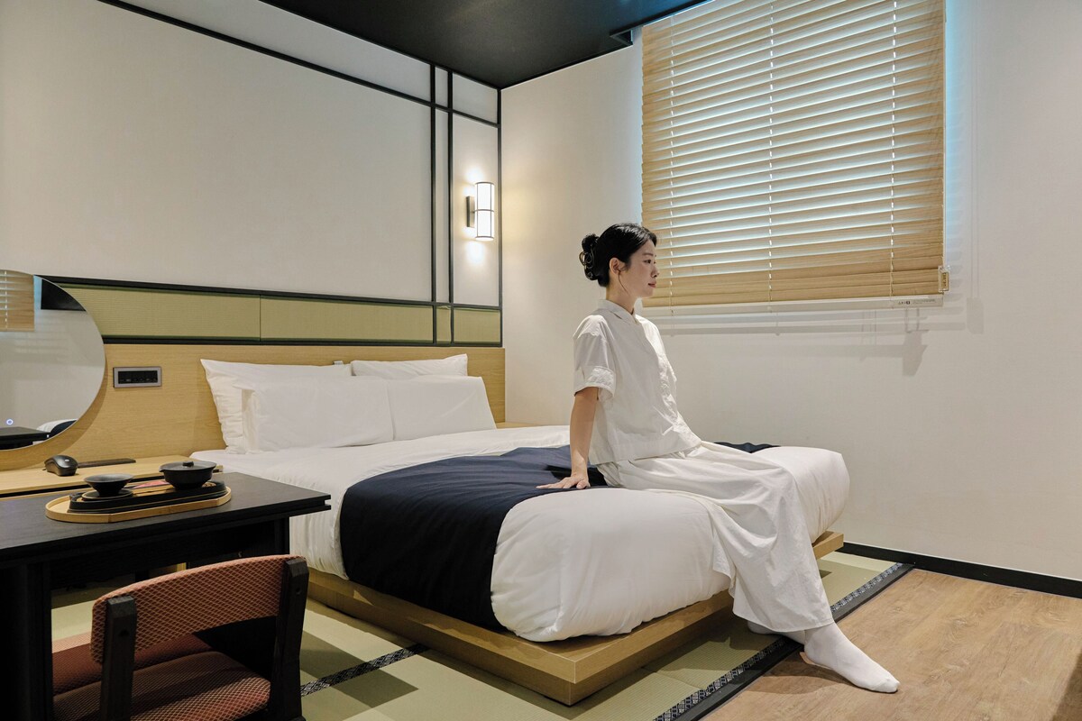 Una habitación de hotel con cama, escritorio, silla y ventana con persianas.