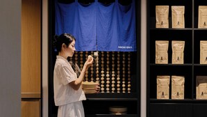 A person holding a bowl in front of a display of wooden bowls and bags labeled 'AMENITY SET' on shelves. - Mitasuya Ryokan Dongducheon Soyosan (Dongducheon)