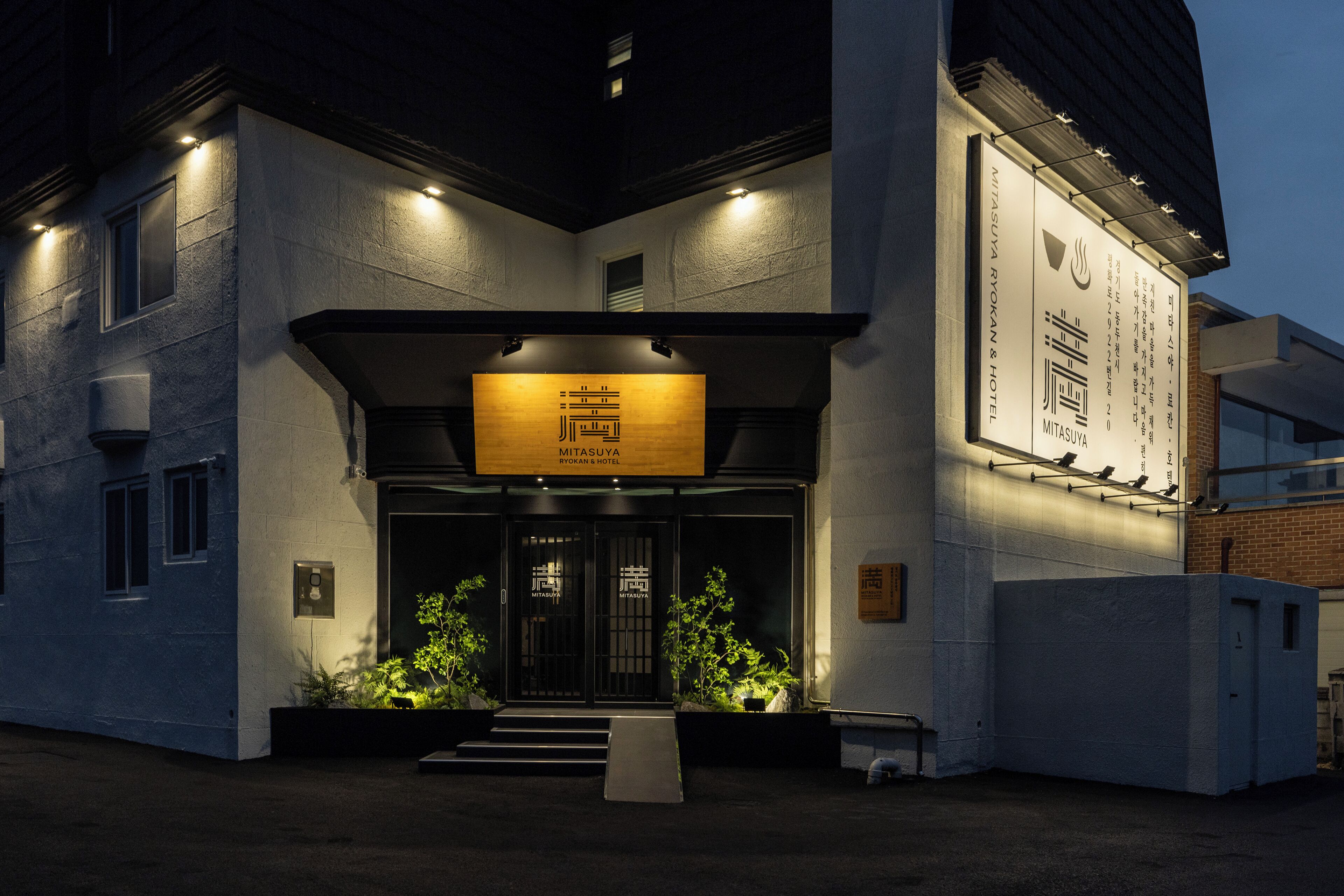 A hotel entrance with a signboard, a staircase, and a small garden area.