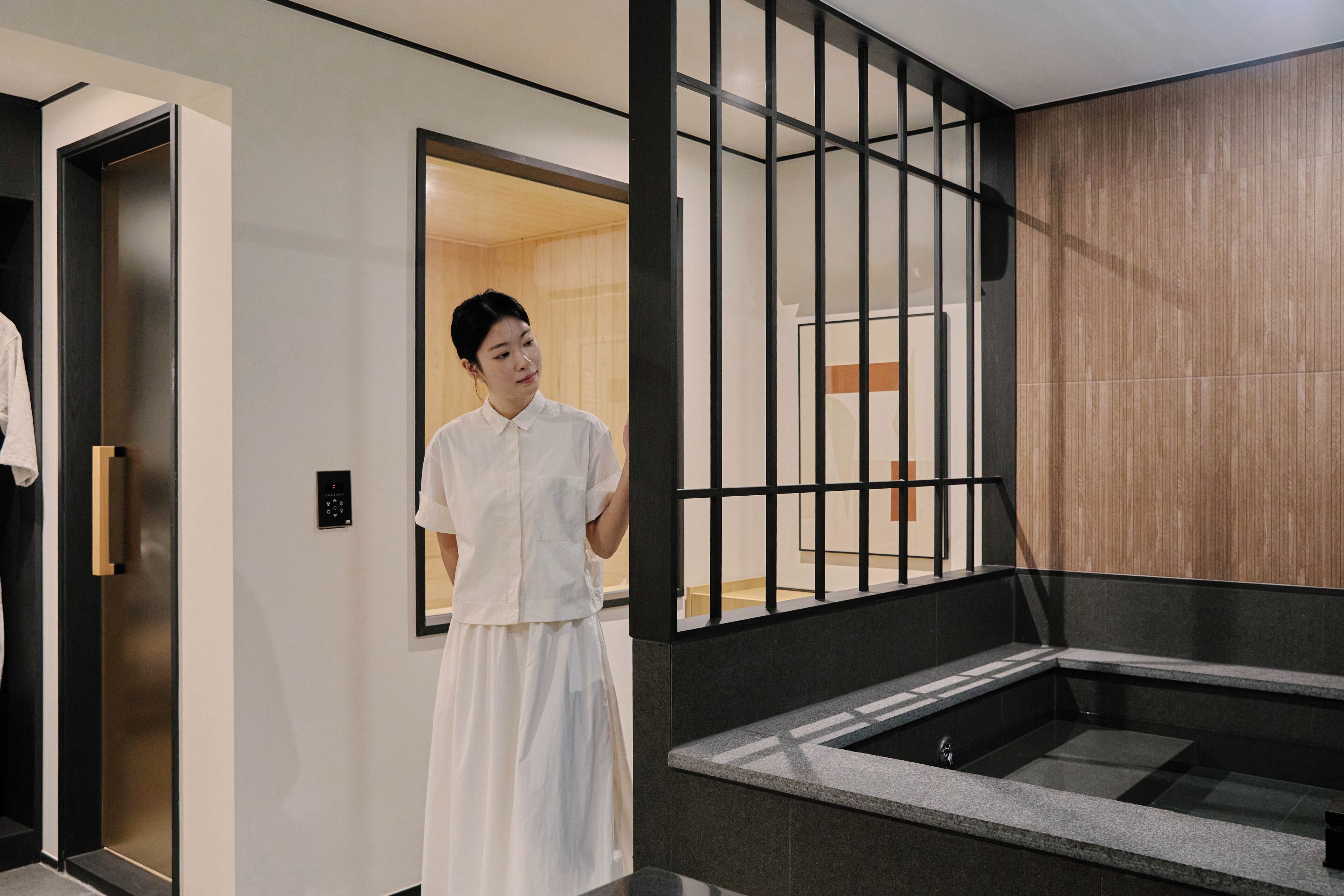 A person standing in a modern hotel lobby with a visible elevator and a reception area.