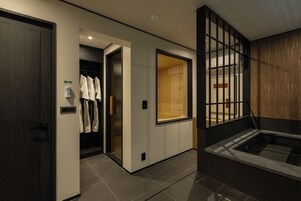 Una habitación de hotel moderna con suelo de madera, un ventanal grande, una bañera integrada y un perchero.