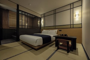 Una habitación de hotel con cama, mesita de noche, silla e iluminación en la pared.