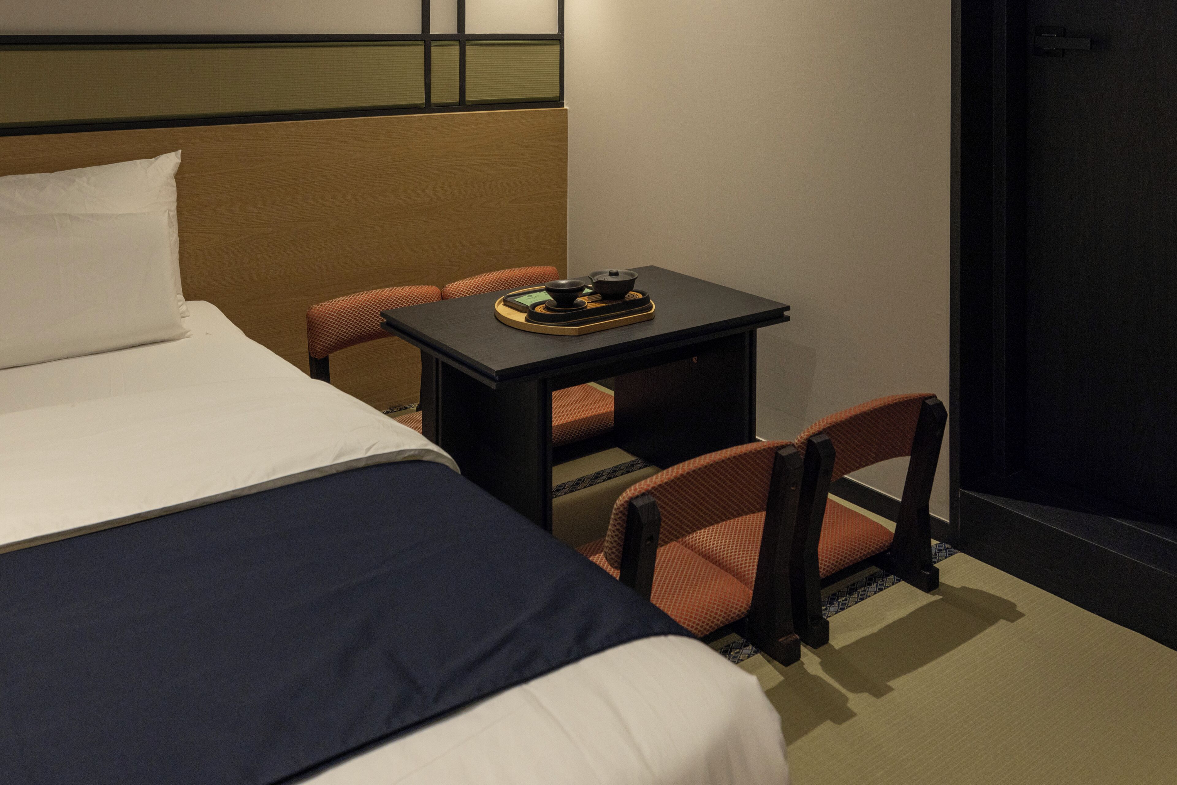 A hotel room with a bed, a small table with a tea set, and two chairs.