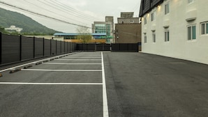 A parking lot with marked spaces, a fence, and buildings in the background. - Mitasuya Ryokan Dongducheon Soyosan (Dongducheon)