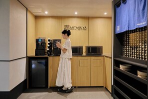 Eine Person in weißer Kleidung steht in einer Küche mit einer Kaffeemaschine, einer Mikrowelle und einer Ansammlung von Kugeln.