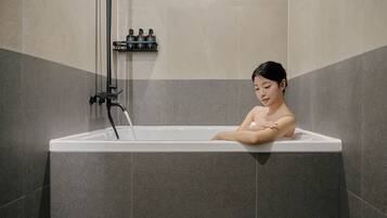 A person relaxing in a bathtub with a water faucet and a shelf with bottles.