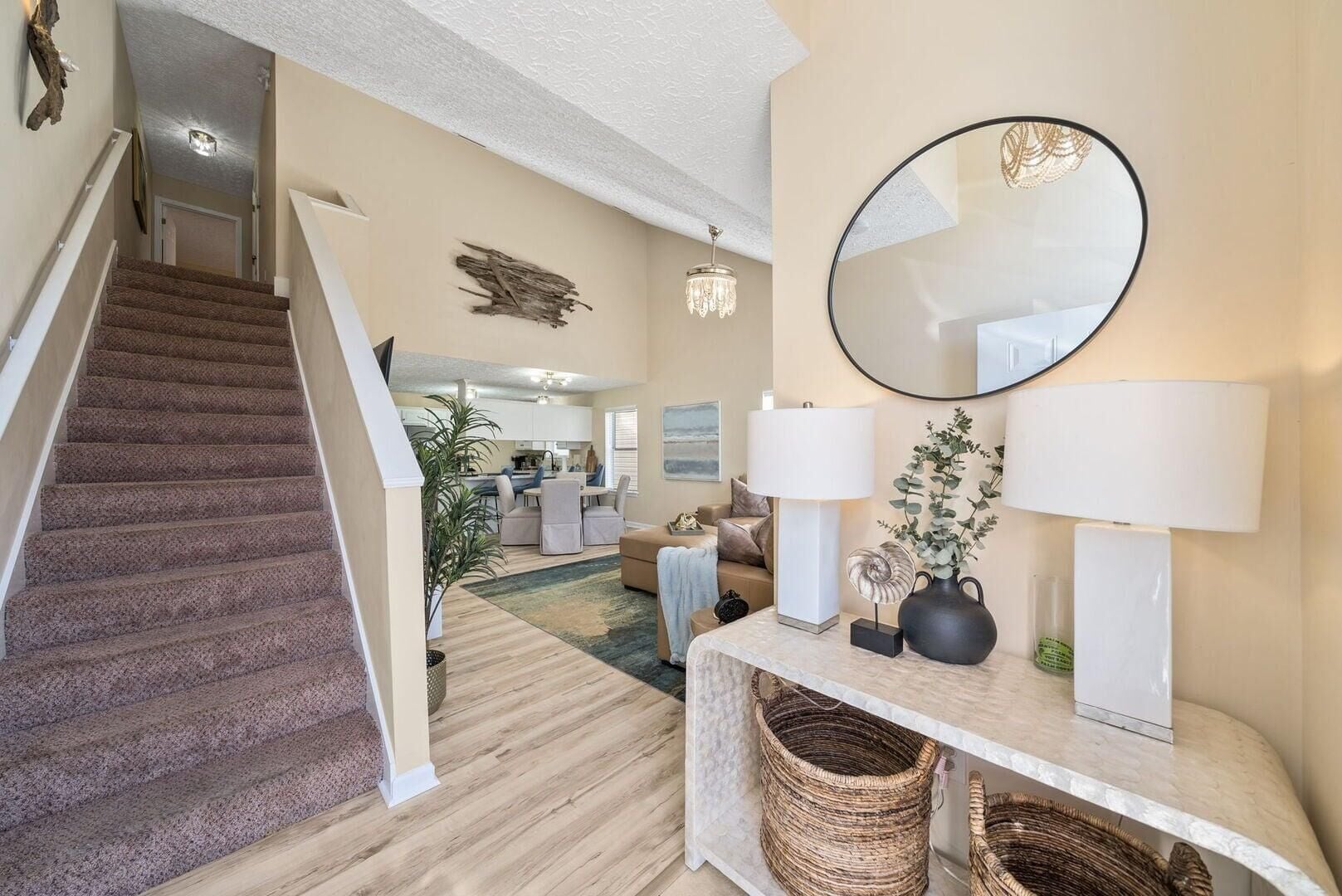 A staircase leading to a living area with a dining table, sofas, and a large mirror.