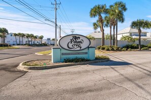 A private residential community sign with a palm tree and a road in the background. - Pet Friendly | Mid-Term & Snowbird Friendly | Near Beach | Central PCB (Panama City Beach)