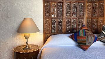 A bed with a patterned pillow, a lamp on a round table, and a wooden headboard with intricate designs.