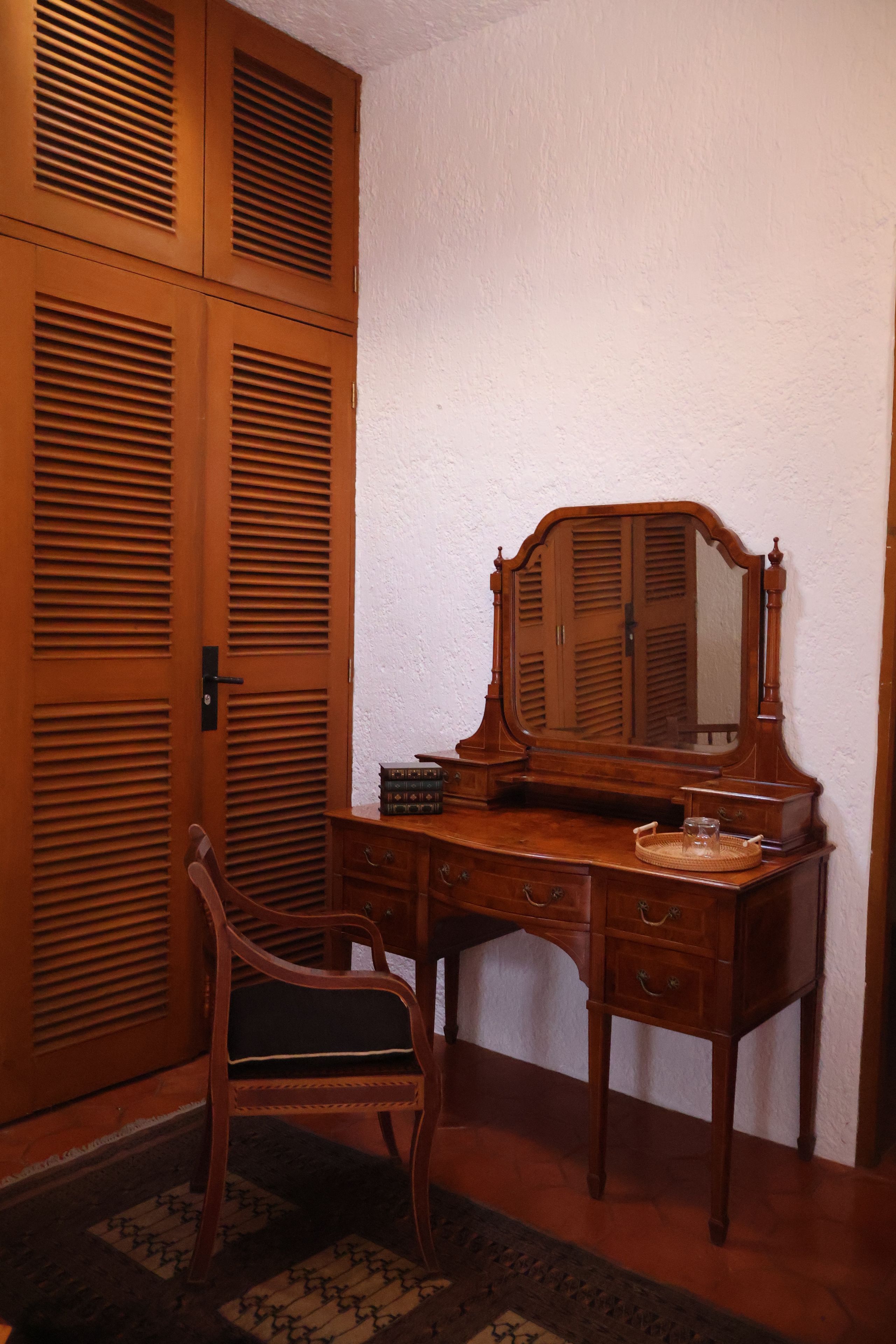 A wooden desk with a mirror, a chair, and a small stack of books.