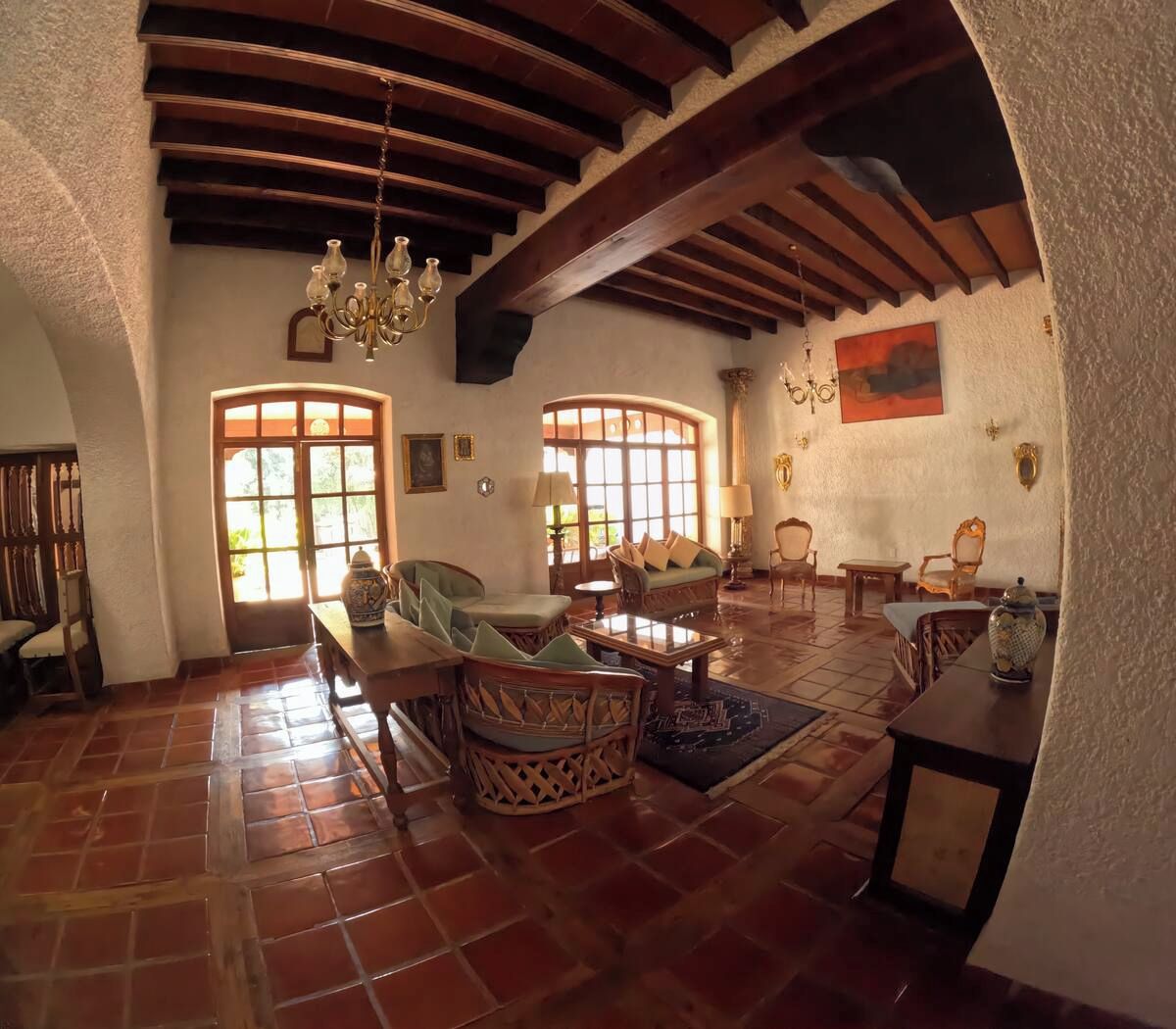 A spacious living area with a high ceiling, wooden beams, and a large window providing natural light.