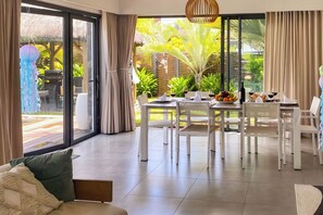 Una moderna zona pranzo con un tavolo apparecchiato per quattro persone, circondata da sedie bianche, con vista su un verdeggiante giardino.