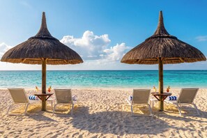 Ein Strand mit zwei Strohdächern und Liegestühlen, jeweils mit einem Getränk.