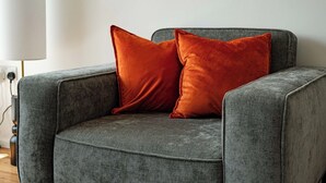 En grå fåtölj med två orange kuddar.