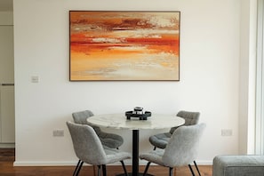 Ein Essbereich mit einem runden Tisch, vier grauen Stühlen und einem großen, abstrakten Gemälde an der Wand.