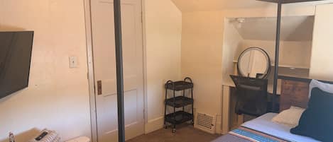A bedroom with a four-poster bed, a bedside table with a lamp, a mirror, and a wardrobe.
