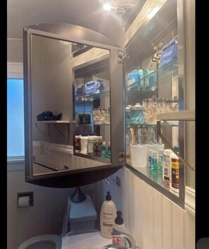 Een badkamer met een grote spiegel, planken met toiletartikelen en een handzeepfles.