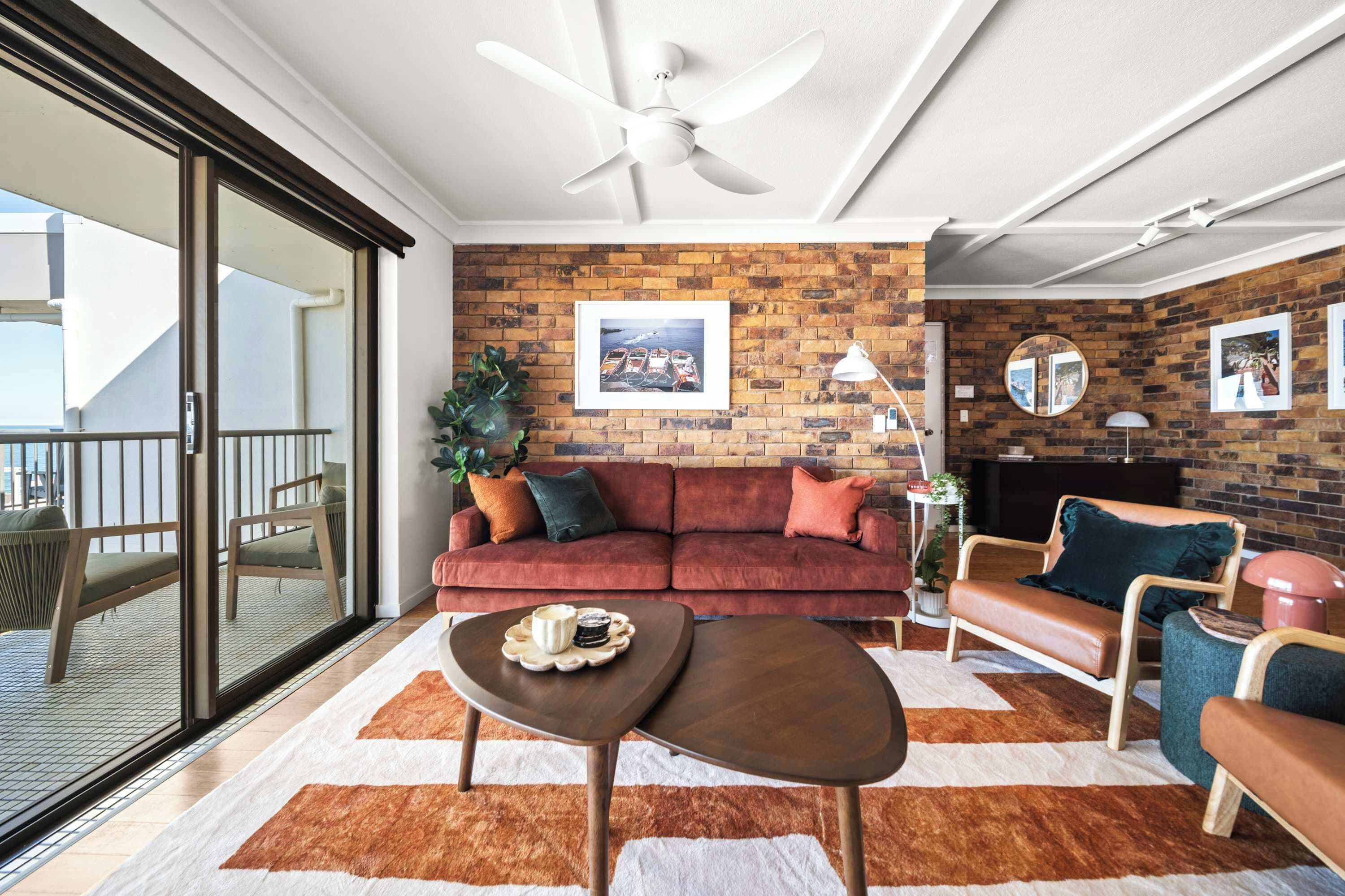 A modern living room with a brick wall, a red sofa, a wooden coffee table, and a ceiling fan.