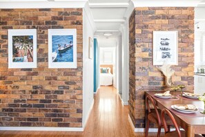 A dining area with a brick wall, wooden floor, and a table set with plates and glasses. - Retro Coastal Retreat w Pool and Kings Beach Views (Caloundra Region)