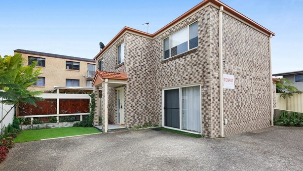 A two-story residential building with a brick facade, a visible garage door, and a sign indicating tenant parking. - Spacious 3-Bed Townhouse Near Broadwater (Labrador)