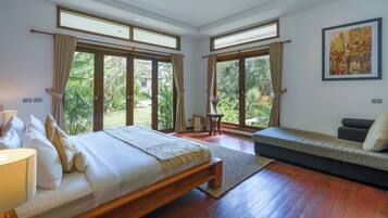 Une chambre spacieuse avec un grand lit, un canapé et une vue sur un jardin grâce à de grandes fenêtres.