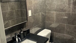 Casa de banho com lavatório de bancada preta, espelho, sanita branca e paredes de mármore escuro.