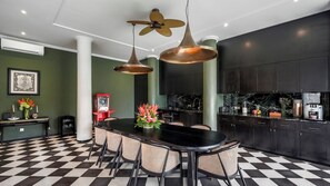 Uma cozinha moderna com piso xadrez preto e branco, armários escuros e uma ilha central com cadeiras.