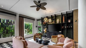 Ein modernes Wohnzimmer mit Schachbrettmuster-Boden, zwei Sofas, einem Couchtisch, einem Deckenventilator und einem großen Fenster mit Blick auf Grünflächen.