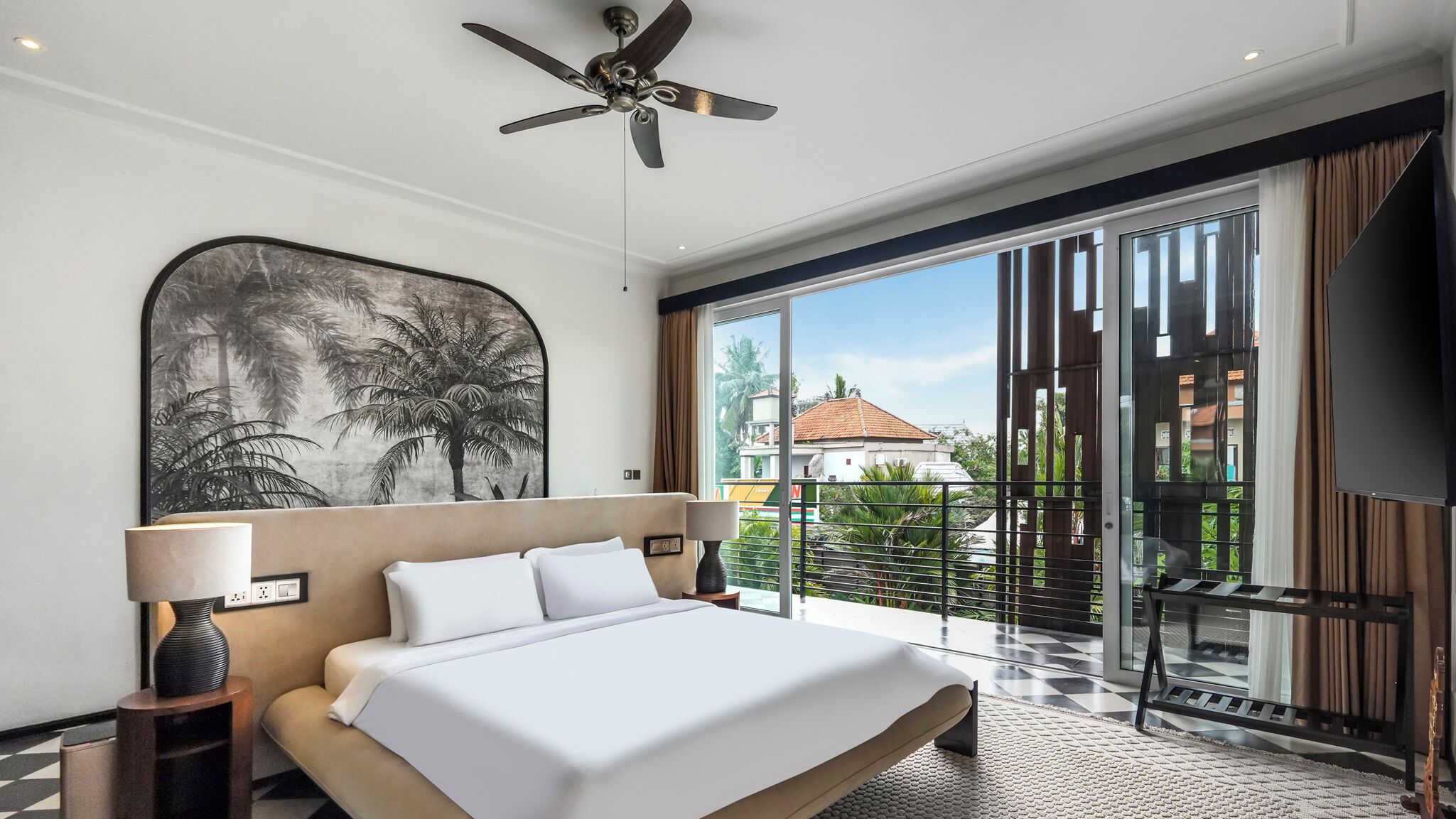 Ein modernes Hotelzimmer mit einem großen Bett, einem Deckenventilator, Blick auf die Stadt und einem Balkon mit Glastür.