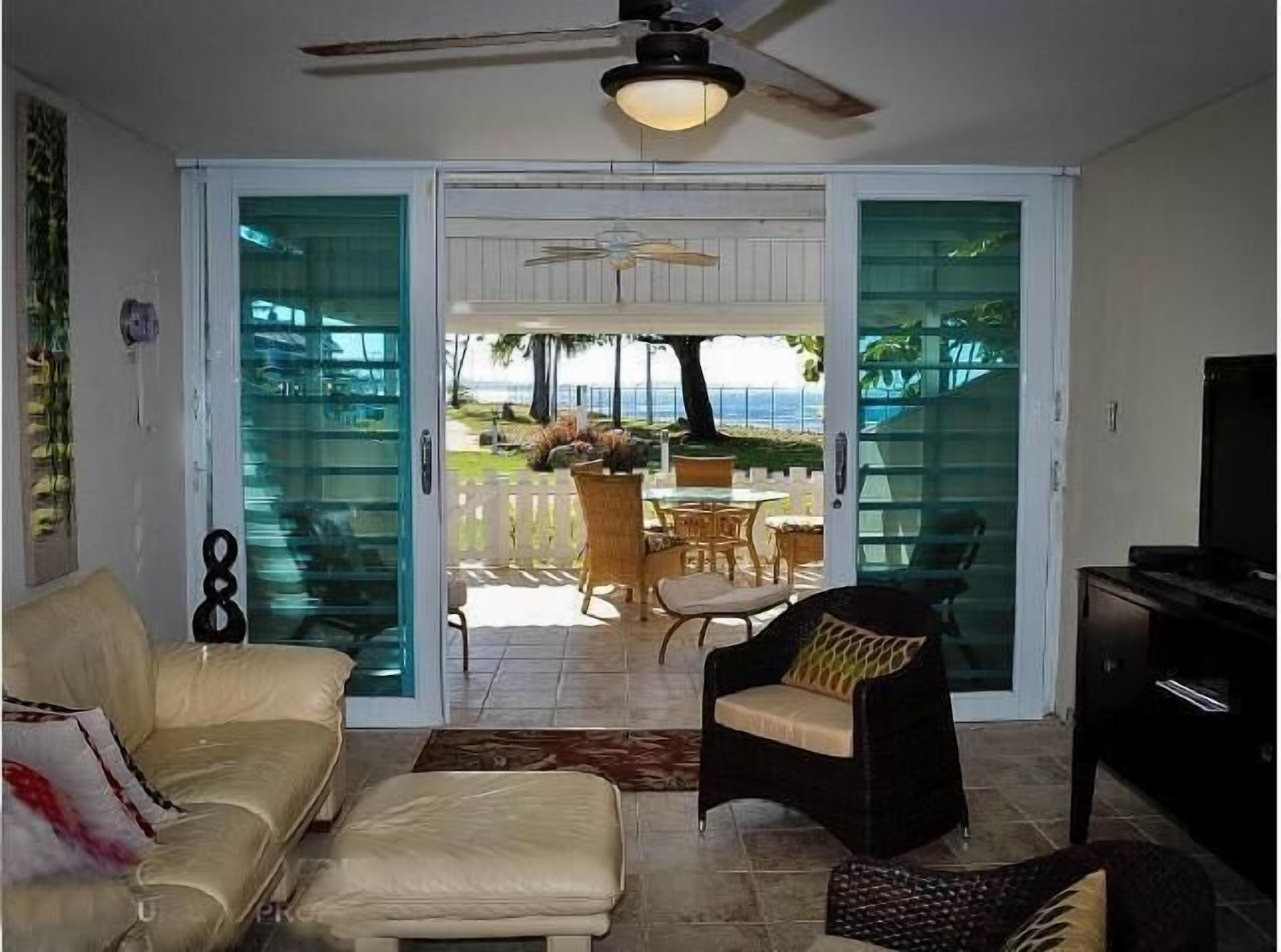 A living room with a sofa, a chair, a television, and a view through a glass door to an outdoor area with a table and chairs.