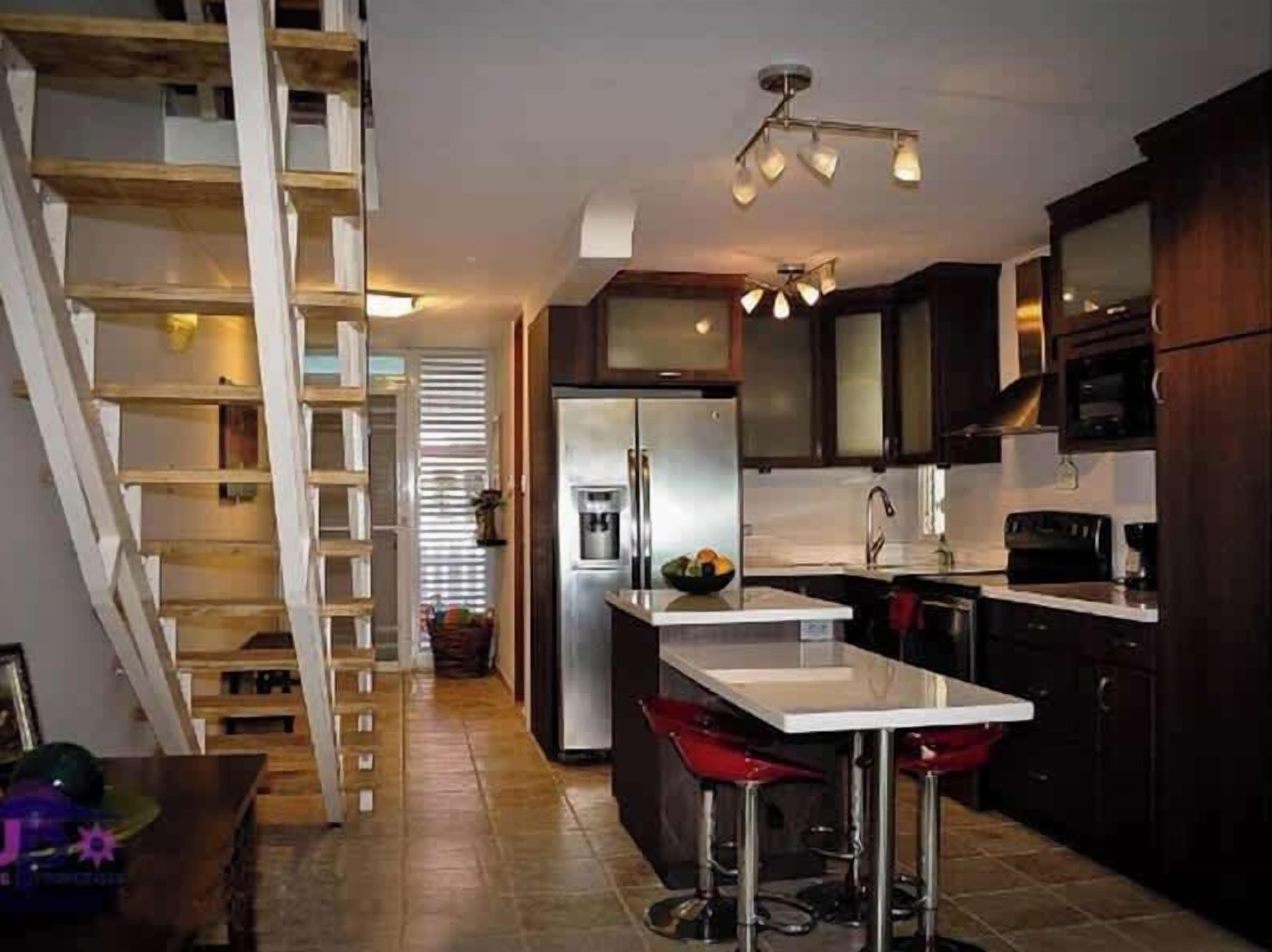 Une cuisine moderne dotée d’un îlot central, d’appareils électroménagers en acier inoxydable et d’un escalier en bois.