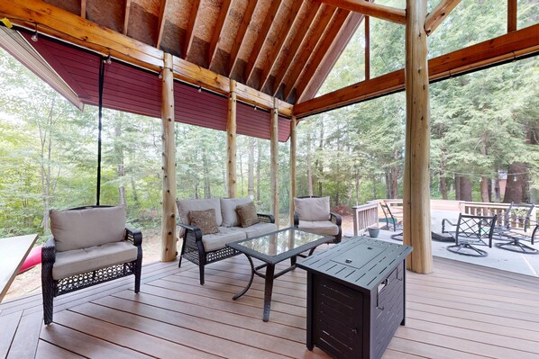 A covered outdoor seating area with a wooden deck, a glass-top table, and cushioned chairs.