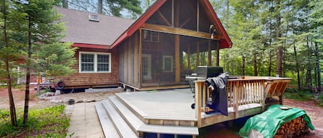 Une cabane dotée d’une terrasse en bois, d’un porche couvert et d’un espace barbecue.