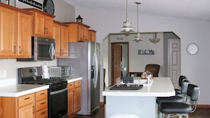 A kitchen with wooden cabinets, stainless steel appliances, a central island with bar stools, and a clock on the wall. - Enjoy a pleasant 3-bedroom Lake House in Scottville besides St Mary's Lake. (Scottville)