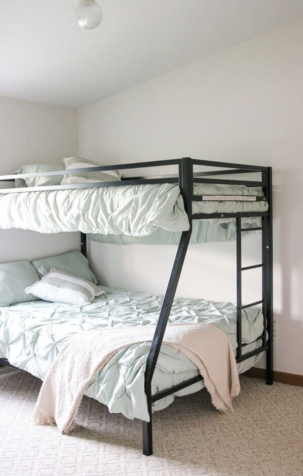 A bunk bed with a mattress and pillows, a bedside table, and a wall-mounted light fixture.