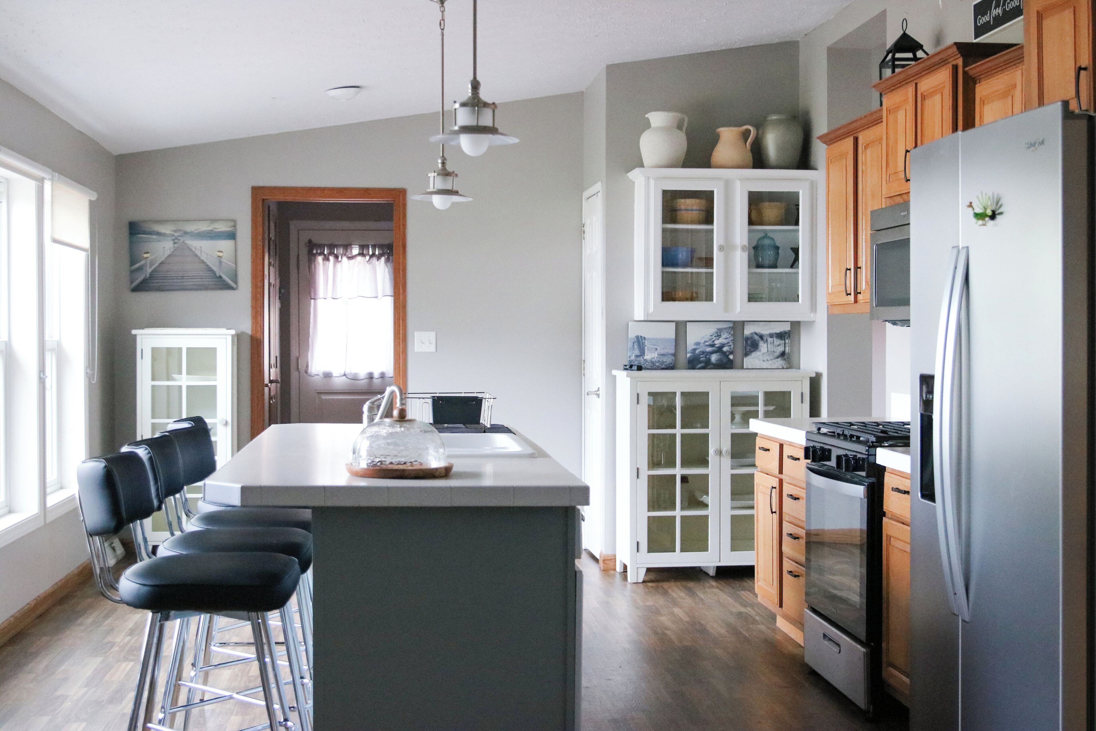 A kitchen with a central island, bar stools, a refrigerator, and wooden cabinets.