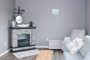 A living room with a stone fireplace, a clock, a sign on the wall, a sofa, and a coffee table.