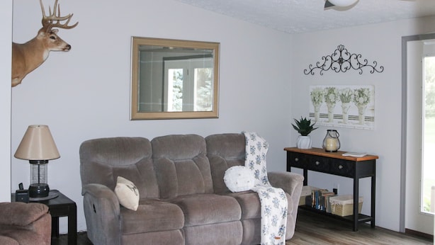 A living room with a grey sofa, a ceiling fan, a deer head decoration, a mirror, and a wall-mounted floral artwork.
