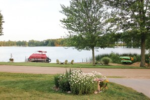 A lakeside setting with a red boat docked, a row of Adirondack chairs, and a small garden with flowers.