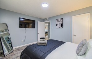 Un dormitorio con cama, espejo, televisión y puerta.
