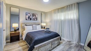Quarto com cama, duas mesas de cabeceira, espelho e janela com cortinas.