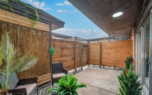 Ein Terrassenbereich im Freien mit Holzlattenzaun, Sitzgelegenheiten und Blumentöpfen.