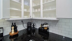 Cozinha com armários brancos, bancada preta e máquina de café.