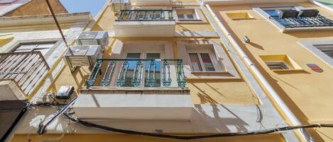 A multi-story building with balconies, air conditioning units, and a clear sky.