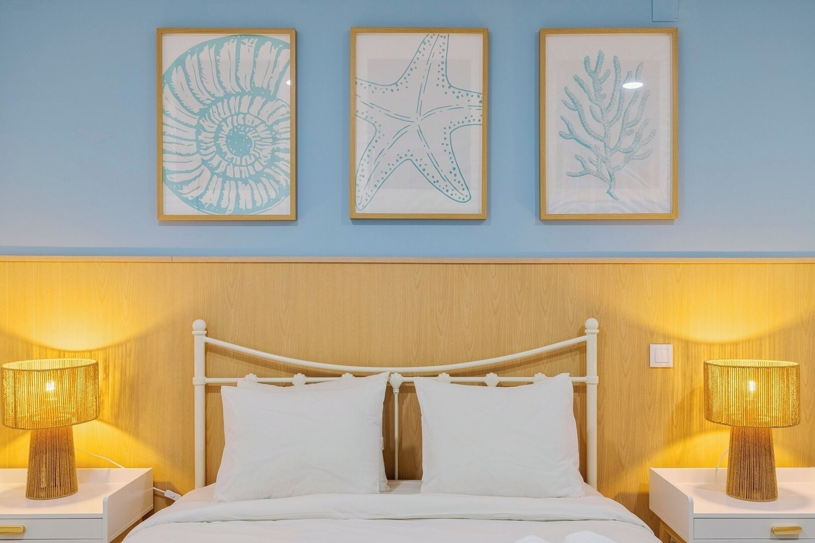 A bed with white bedding, two bedside lamps, and three framed wall art pieces above the bed.