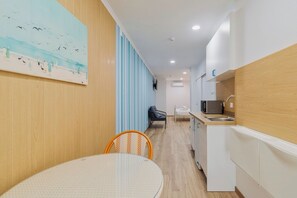 A modern kitchen with white cabinets, a microwave, and a sink. There is a dining area with a round table and chairs. A painting of birds and people is on the wall. - Bocage Blue Heaven I, By Home Match (Setúbal)