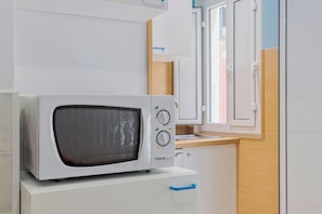 A white microwave on a white cabinet in a kitchen with wooden cabinets and a window.