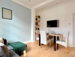 A modern living room with a dining area, a flat-screen TV mounted on the wall, and a bookshelf with decorative items. - Islington 2 bedroom terrace Apartment by PrimeCityHosts (London)
