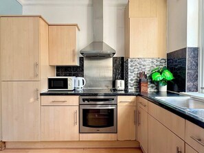 A modern kitchen with wooden cabinets, a stainless steel range hood, a microwave, a toaster, and a built-in oven. - Islington 2 bedroom terrace Apartment by PrimeCityHosts (London)
